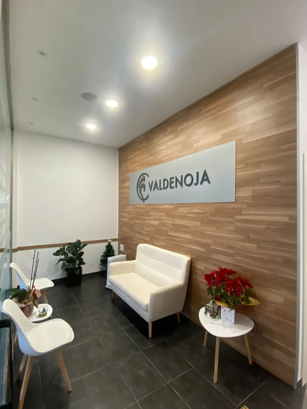 Zona de espera de la Clínica Podológica Valdenoja, con su rótulo y pared de madera